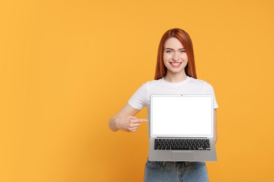 Photo of Smiling young woman showing laptop on yellow background, space for text