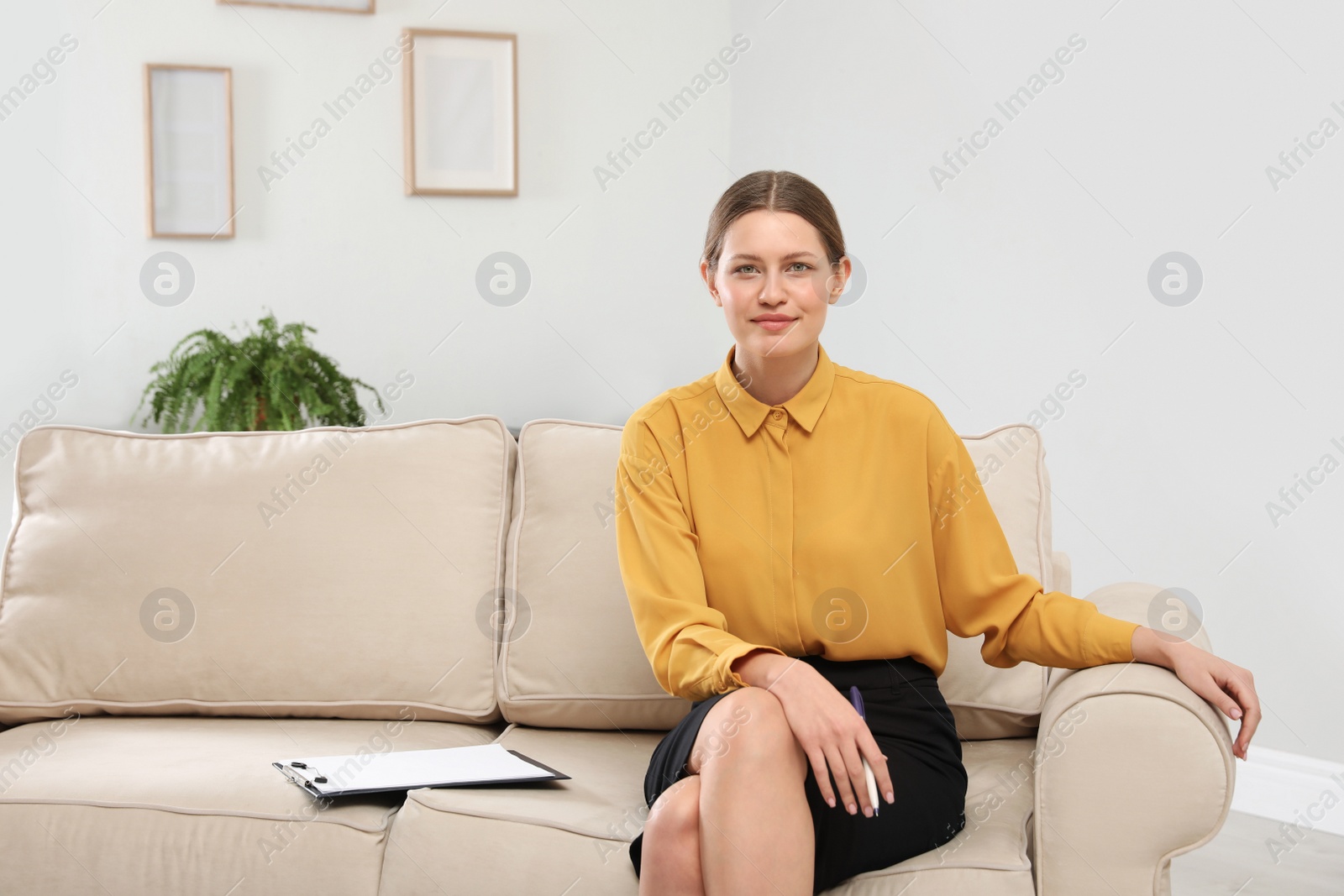 Photo of Professional psychotherapist with clipboard on sofa in office