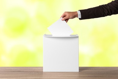 Man putting his vote into ballot box on color background, closeup