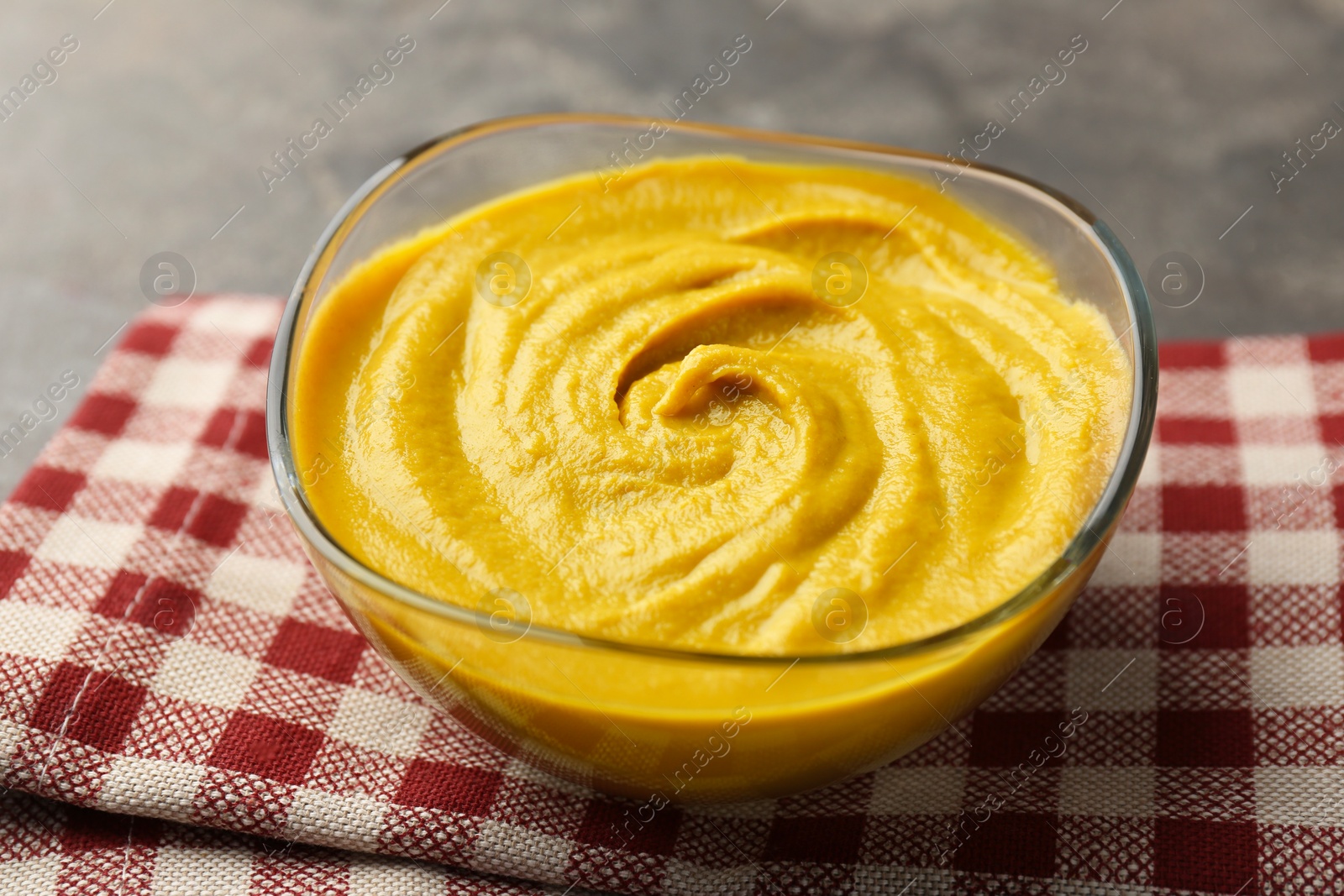 Photo of Tasty mustard sauce in glass bowl on grey table, closeup