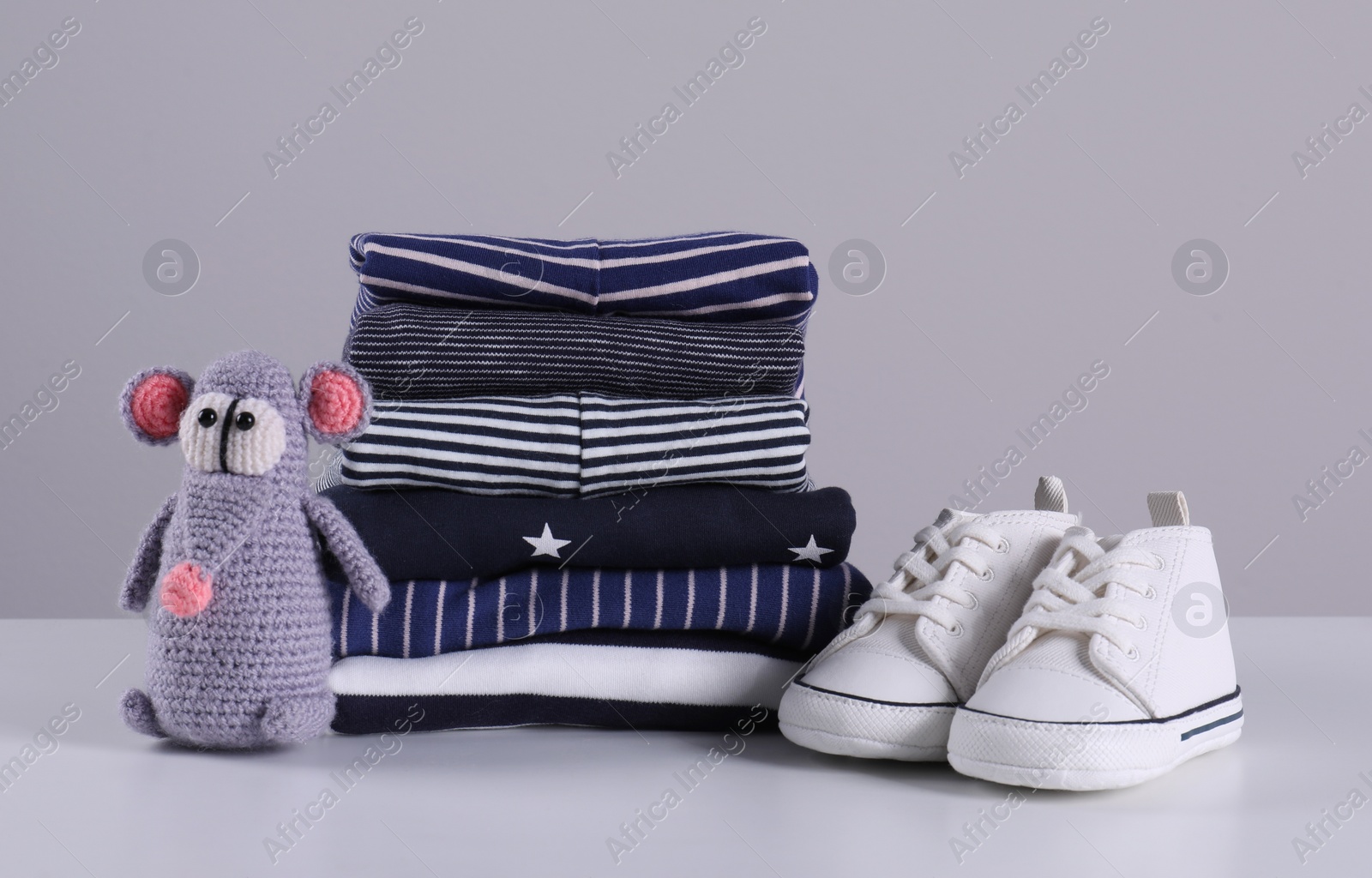 Photo of Stack of clean baby's clothes, toy and small shoes on table against light grey background