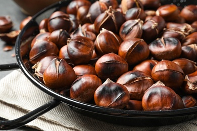 Photo of Delicious roasted edible chestnuts in frying pan on table, closeup