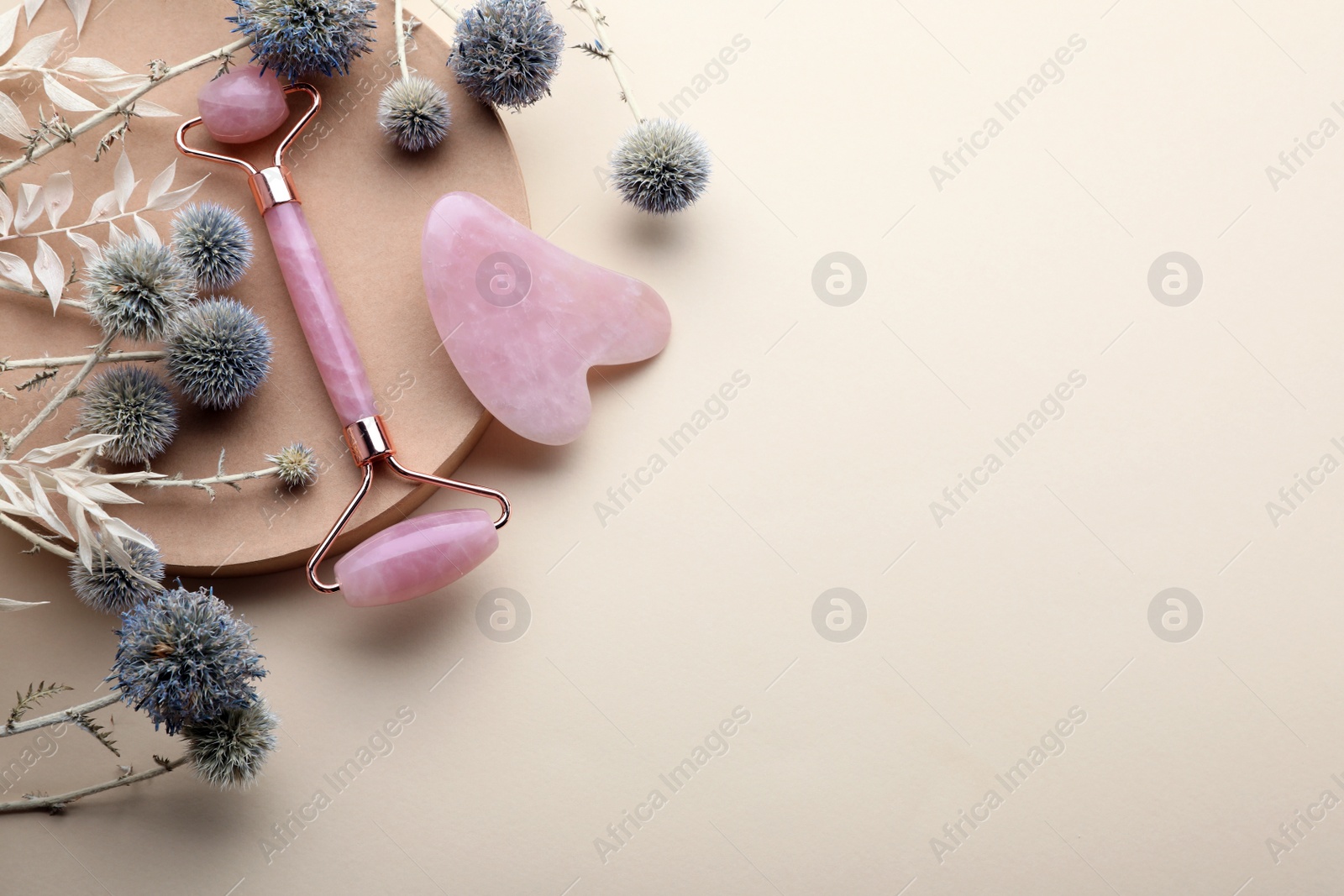 Photo of Flat lay composition with rose quartz gua sha tool and facial roller on beige background. Space for text