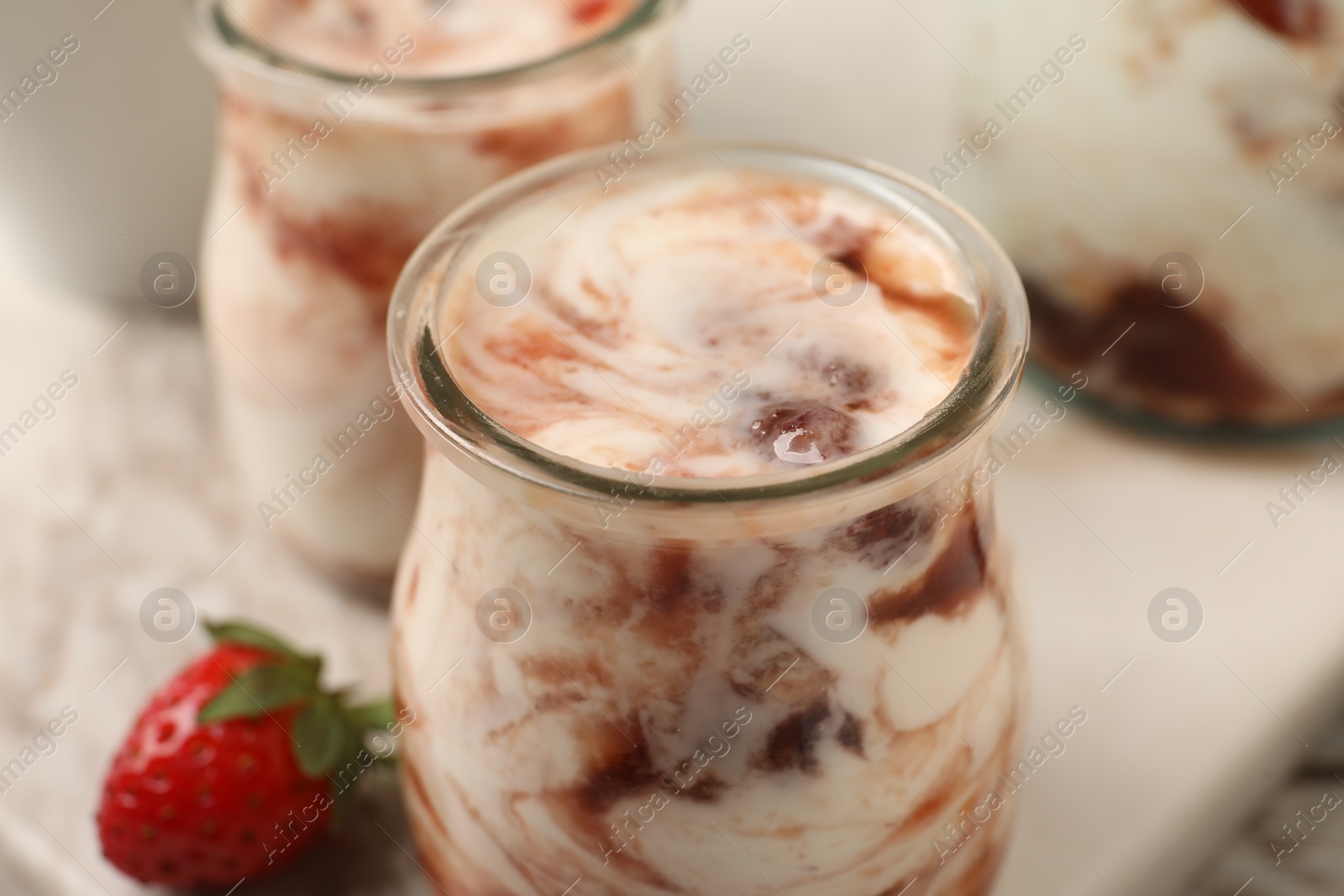 Photo of Tasty yoghurt with jam and strawberry on white marble board, closeup