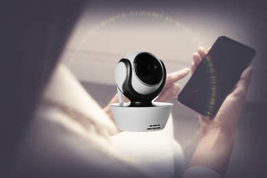 Image of CCTV camera and woman with smartphone indoors, closeup