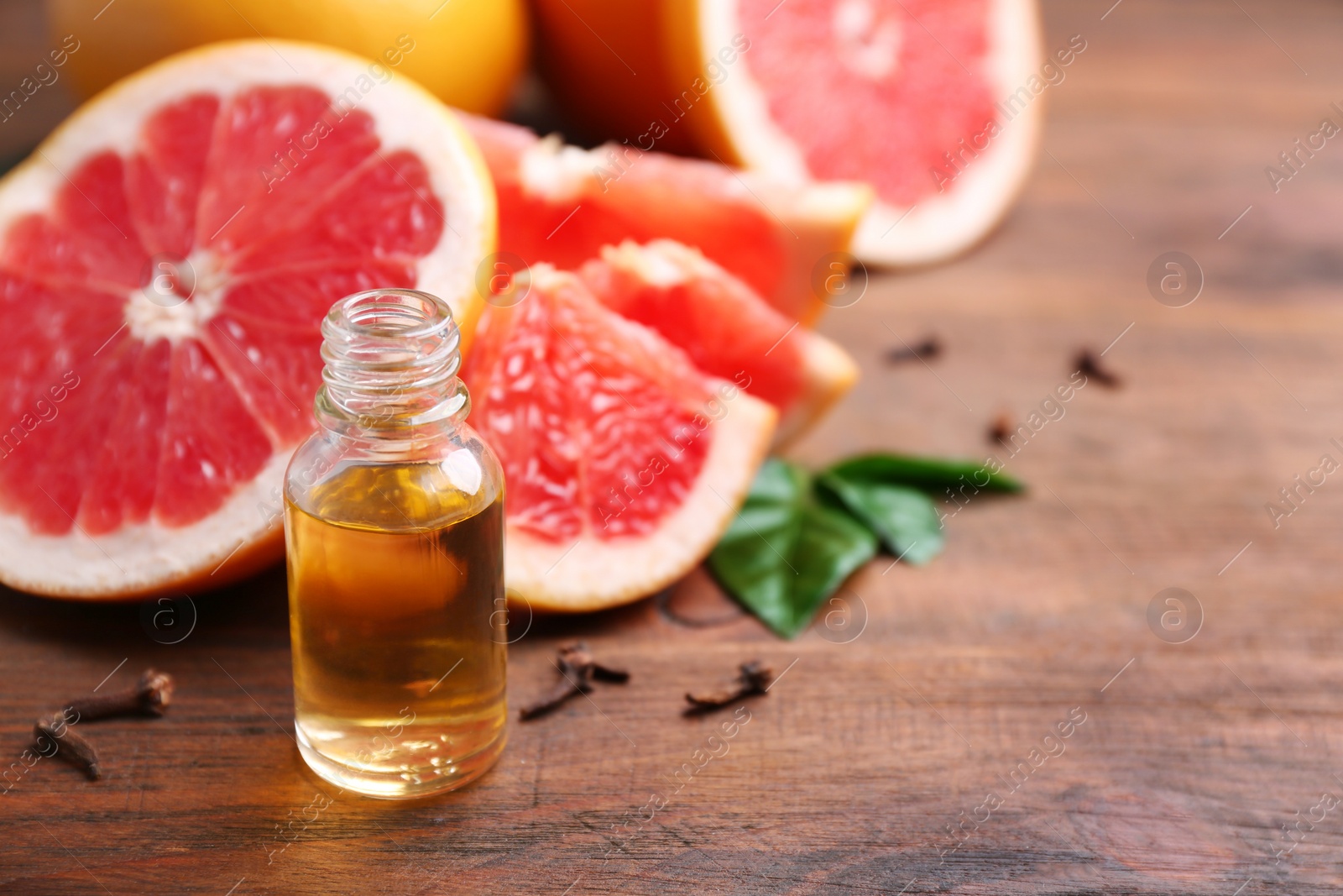 Photo of Bottle of essential oil and fresh grapefruit on wooden table, space for text