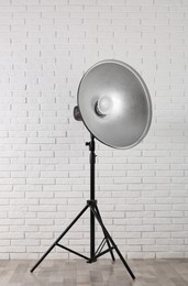 Professional beauty dish reflector on tripod near white brick wall in room. Photography equipment