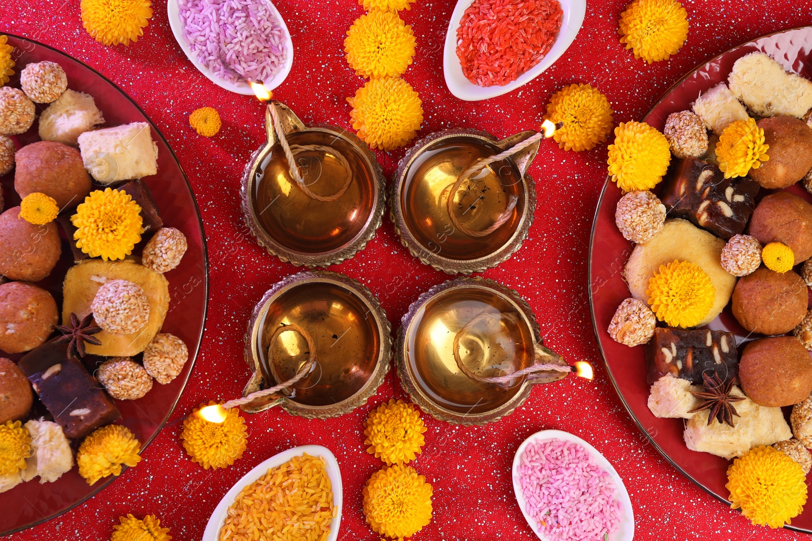 Photo of Diwali celebration. Flat lay composition with diya lamps and tasty Indian sweets on shiny red table