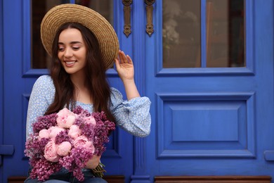 Photo of Beautiful woman with bouquet of spring flowers near blue wooden doors, space for text