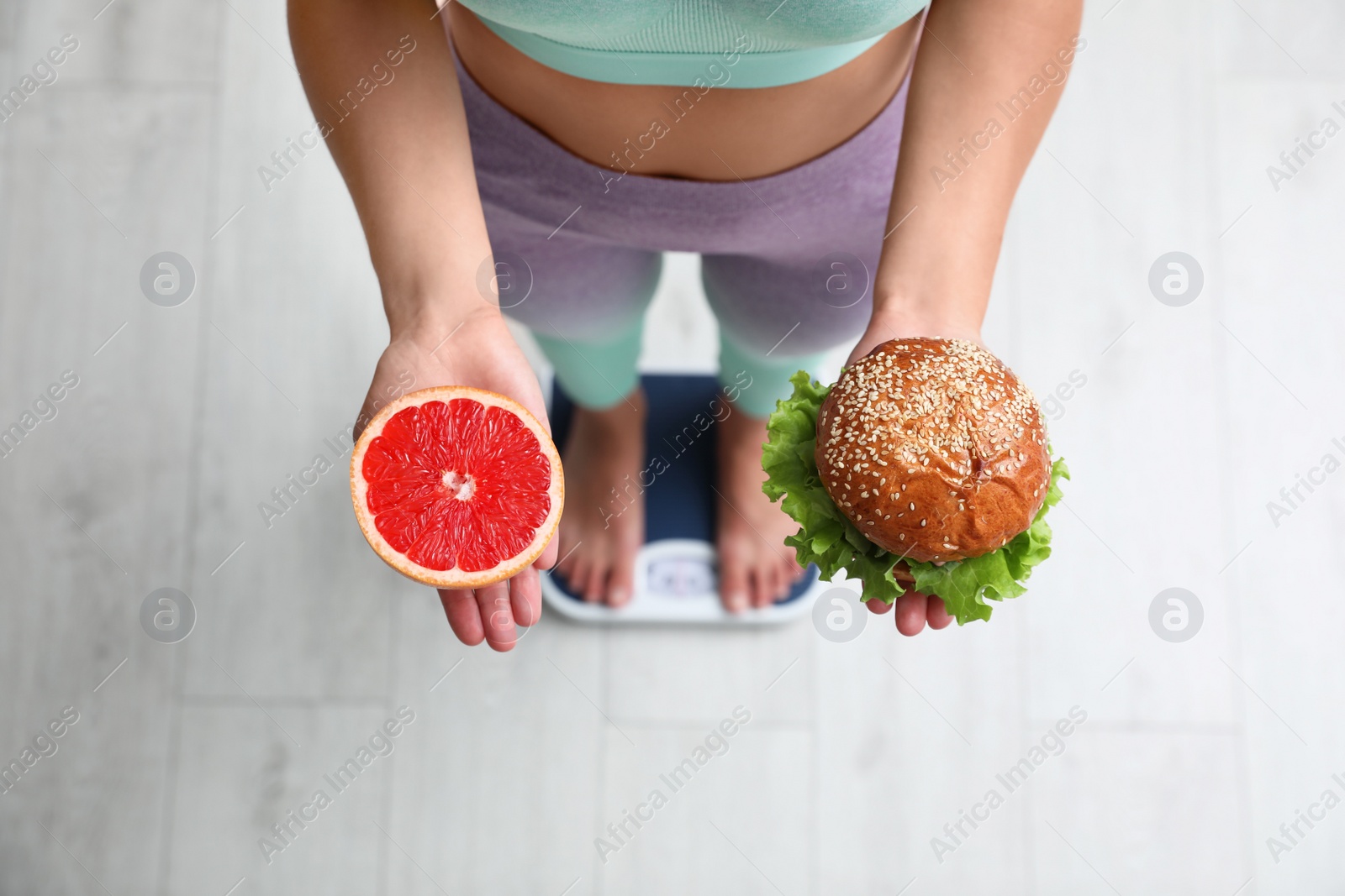 Photo of Choice concept. Top view of woman with grapefruit and burger standing on scales, closeup