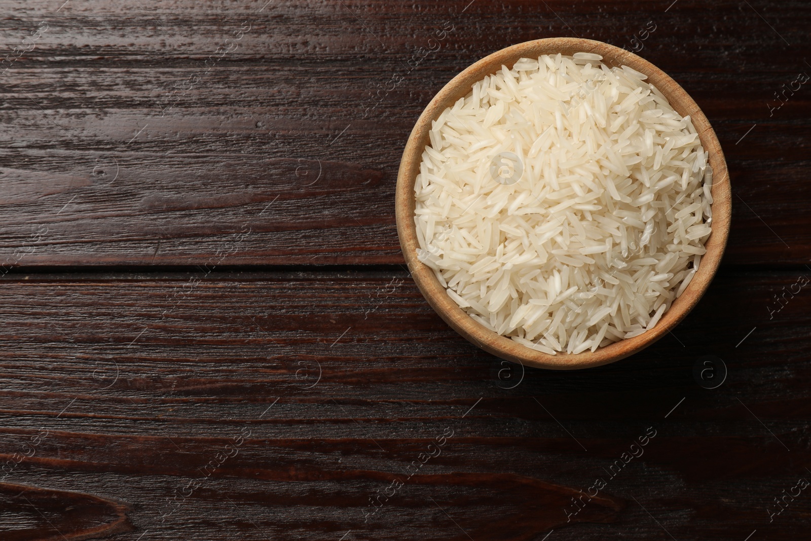 Photo of Raw basmati rice in bowl on wooden table, top view. Space for text