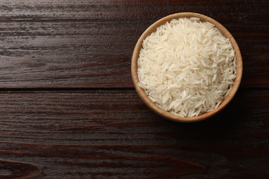 Photo of Raw basmati rice in bowl on wooden table, top view. Space for text