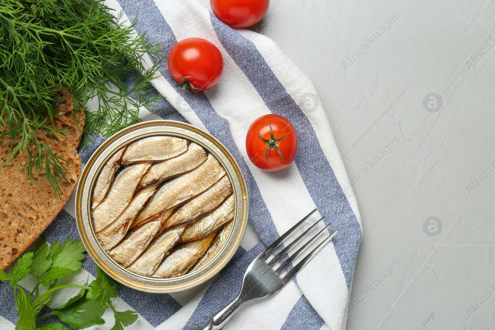 Photo of Canned sprats, herbs, tomatoes, bread and fork on light table, flat lay. Space for text