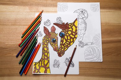 Colored and blank drawings with pencils on wooden table, flat lay