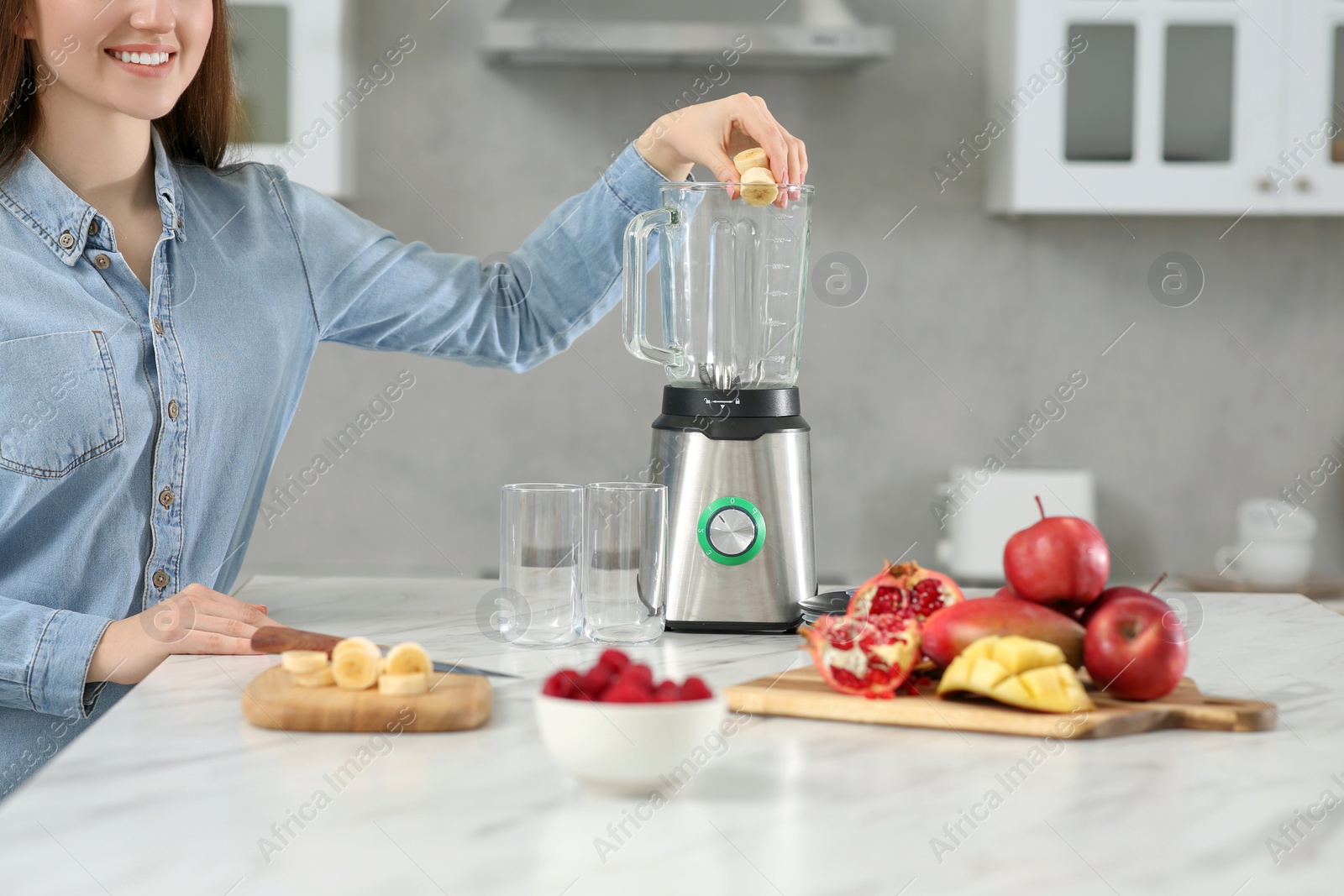 Photo of Beautiful young woman adding banana into blender for tasty smoothie in kitchen, closeup