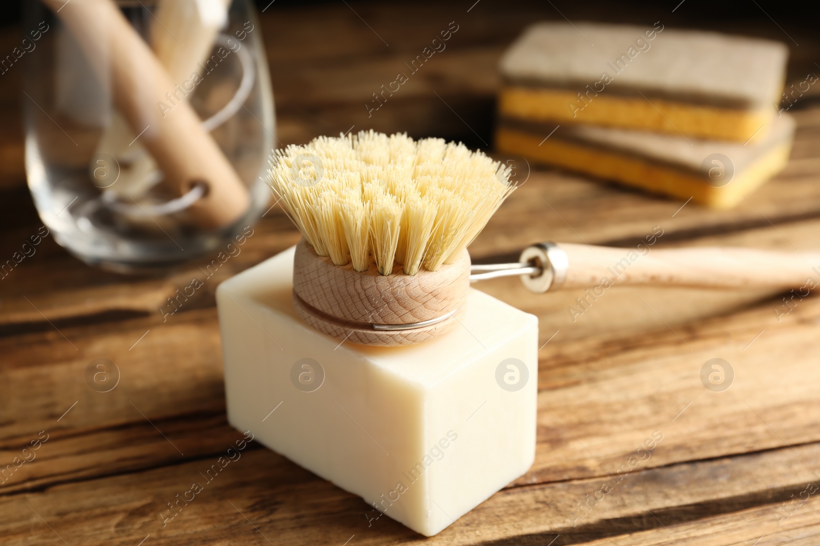 Photo of Cleaning brush and soap bar for dish washing on wooden table, closeup
