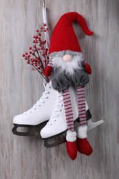 Photo of Pair of ice skates with Christmas gnome and decorative branches hanging on wooden wall
