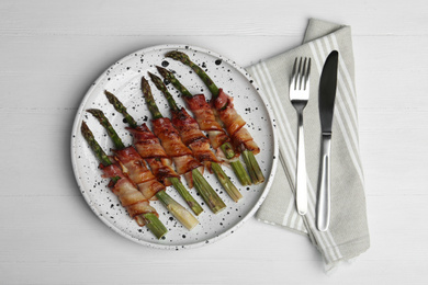 Oven baked asparagus wrapped with bacon on white wooden table, flat lay