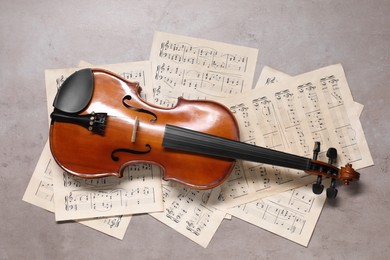 Violin and music sheets on grey table, top view