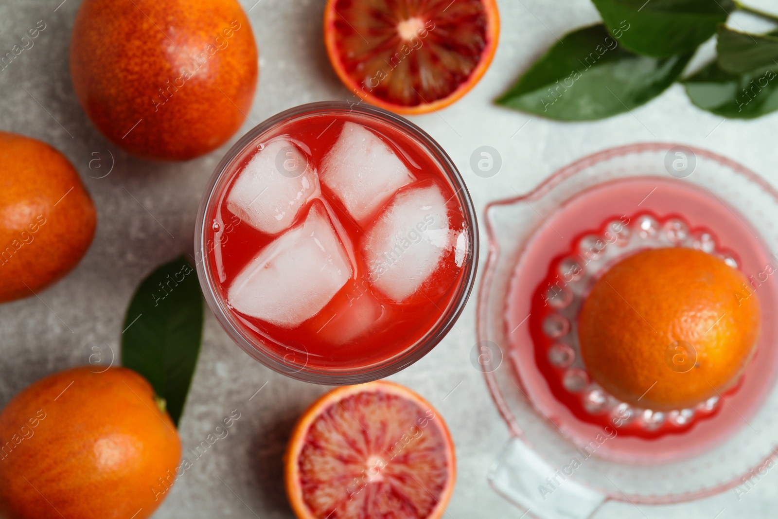 Photo of Tasty sicilian orange juice with ice cubes, fruits and squeezer on light grey table, flat lay