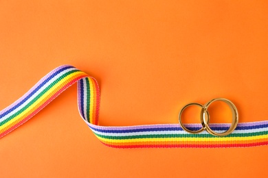 Photo of Wedding rings and rainbow ribbon on color background, top view. Gay symbol