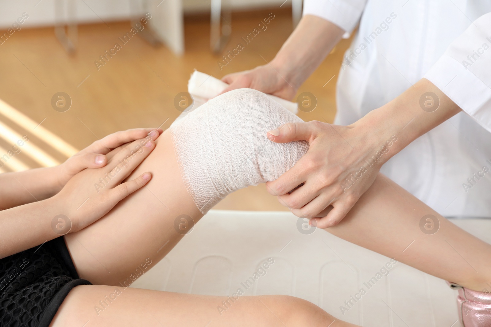 Photo of Doctor applying medical bandage to little patient's injured knee in clinic, closeup