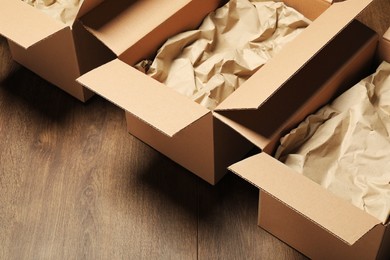 Photo of Open cardboard boxes with crumpled paper on wooden floor. Packaging goods