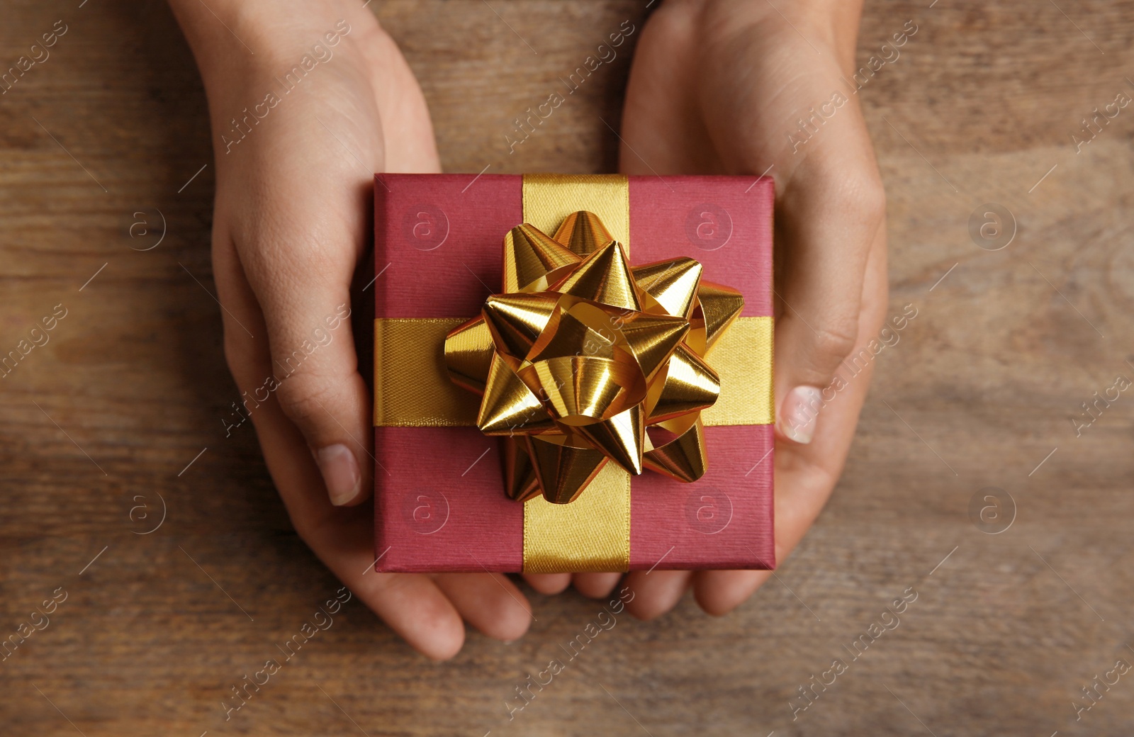 Photo of Woman holding beautiful gift box over wooden table, top view