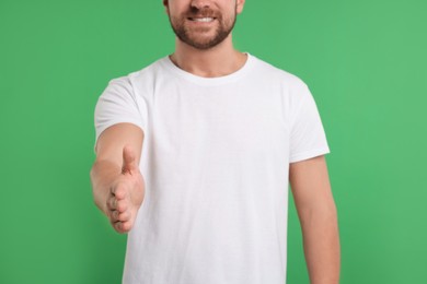 Photo of Man welcoming and offering handshake on green background, closeup
