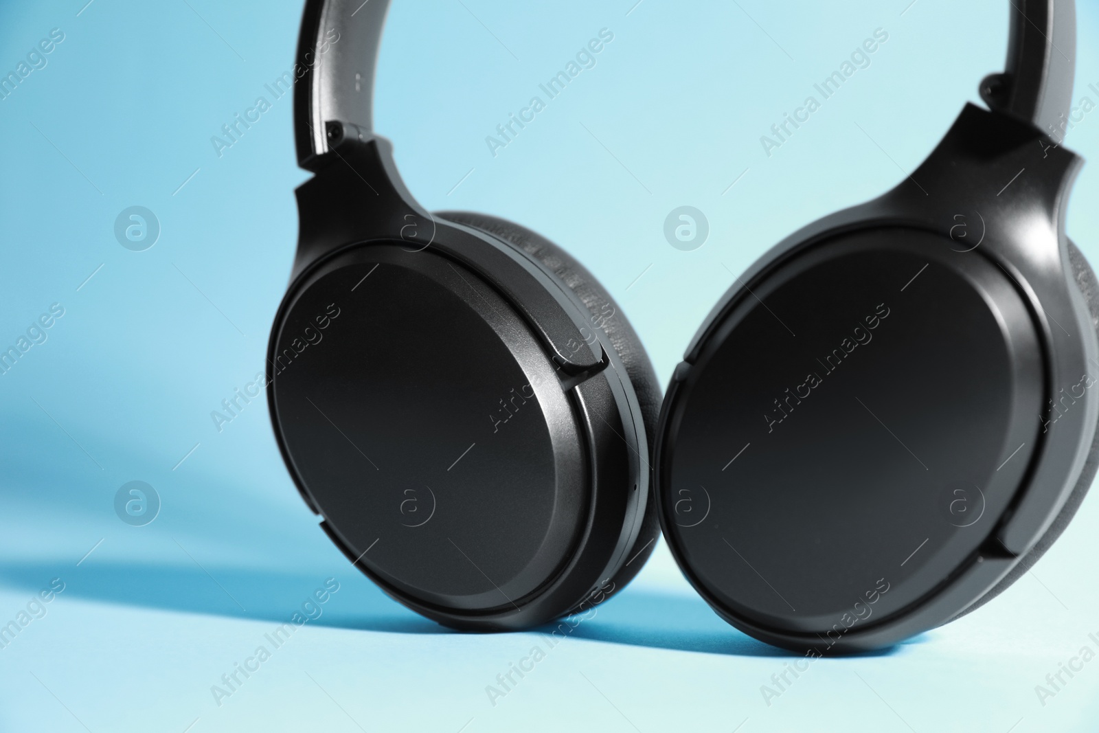 Photo of Modern wireless headphones on light blue background, closeup