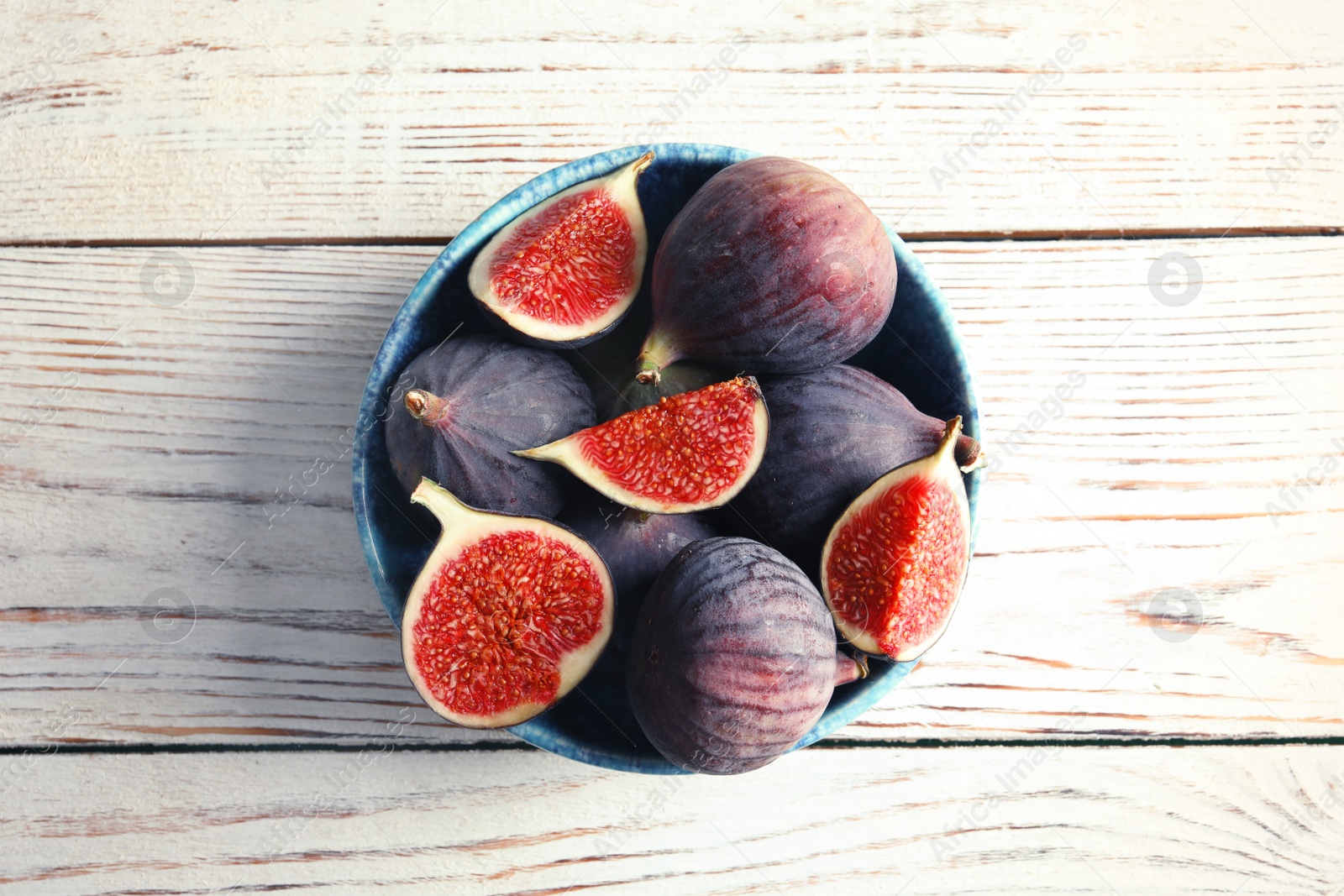 Photo of Bowl with fresh ripe figs on wooden background, top view