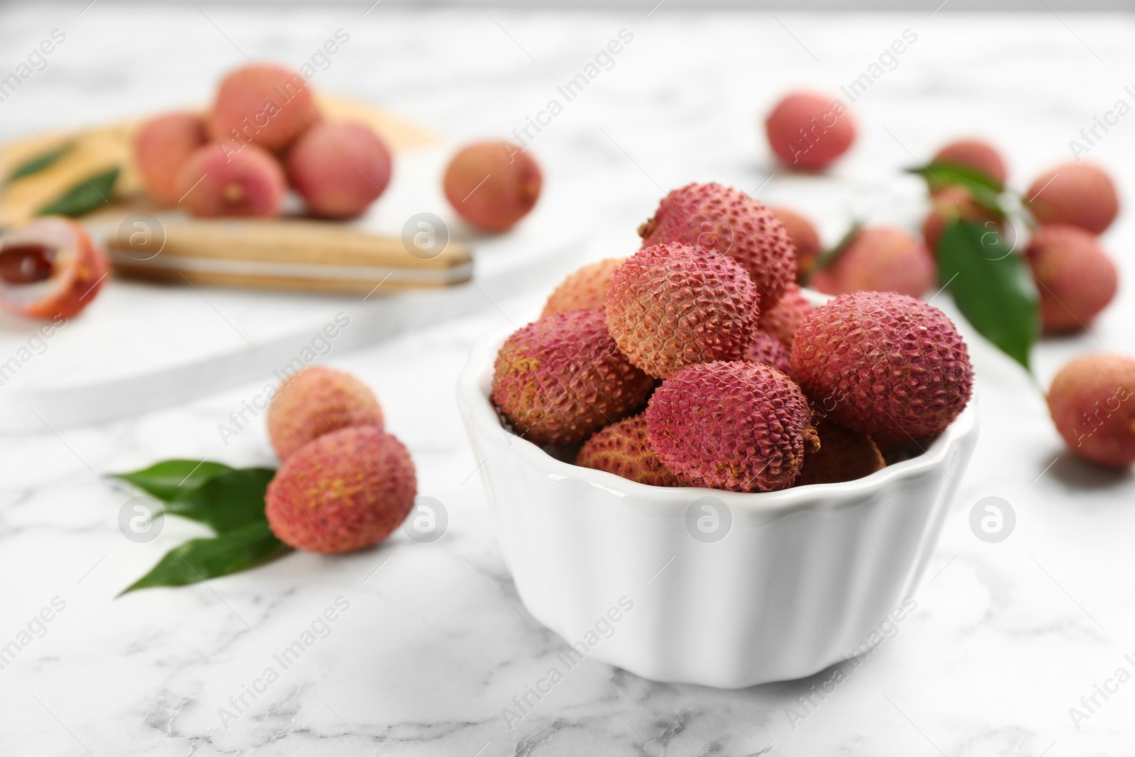 Photo of Fresh ripe lychee fruits in ceramic bowl on white marble table. Space for text