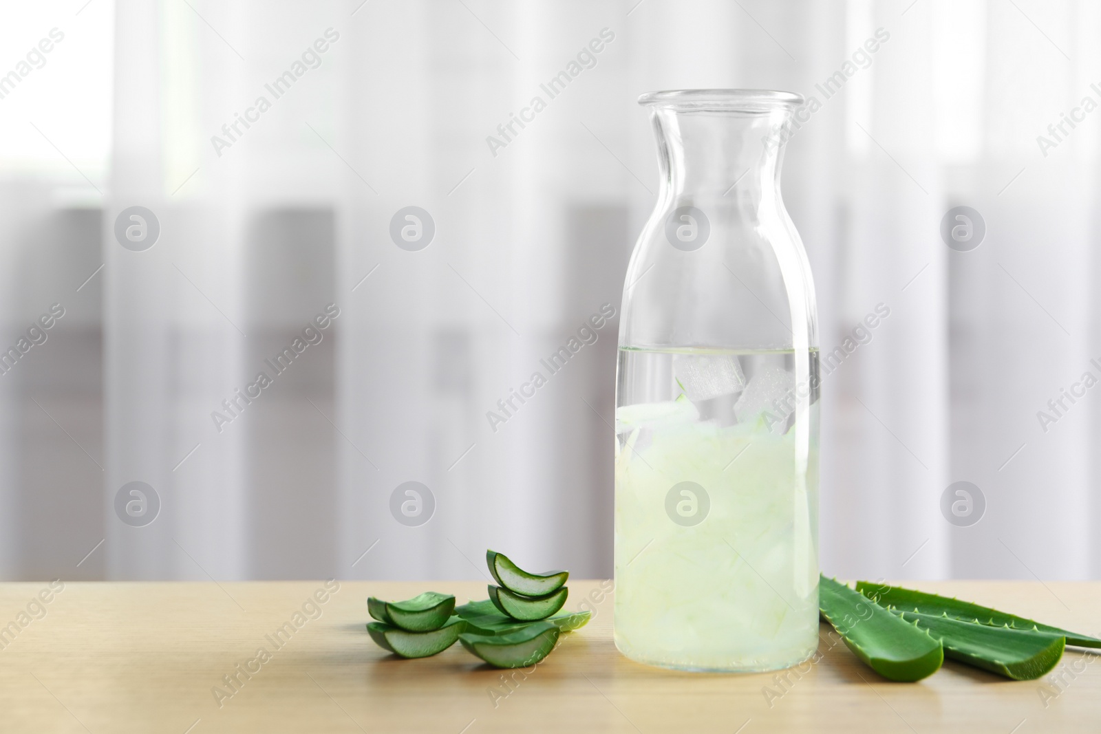 Photo of Bottle with fresh aloe vera juice and green leaves on wooden table indoors. Space for text