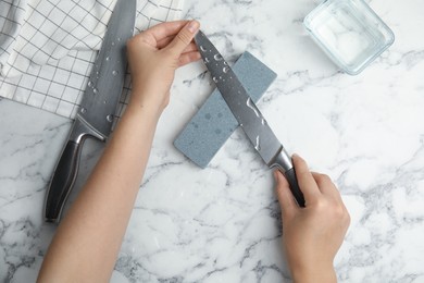 Photo of Woman sharpening knife at white marble table, top view