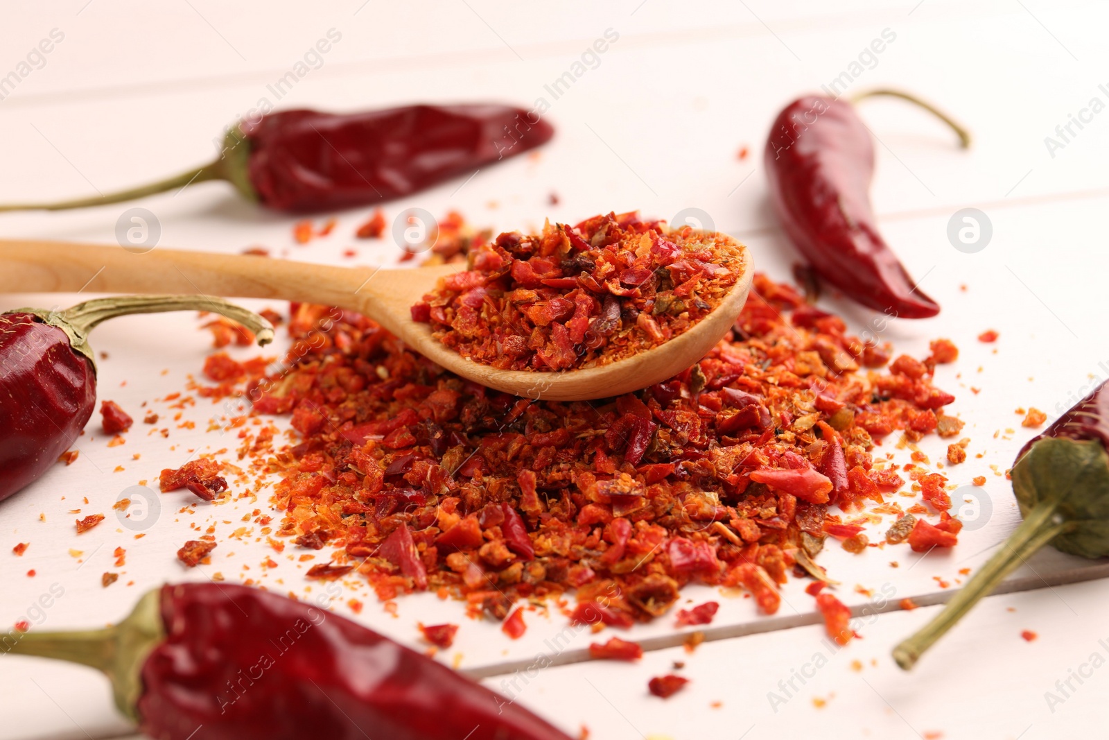 Photo of Chili pepper flakes and pods on white wooden table, closeup