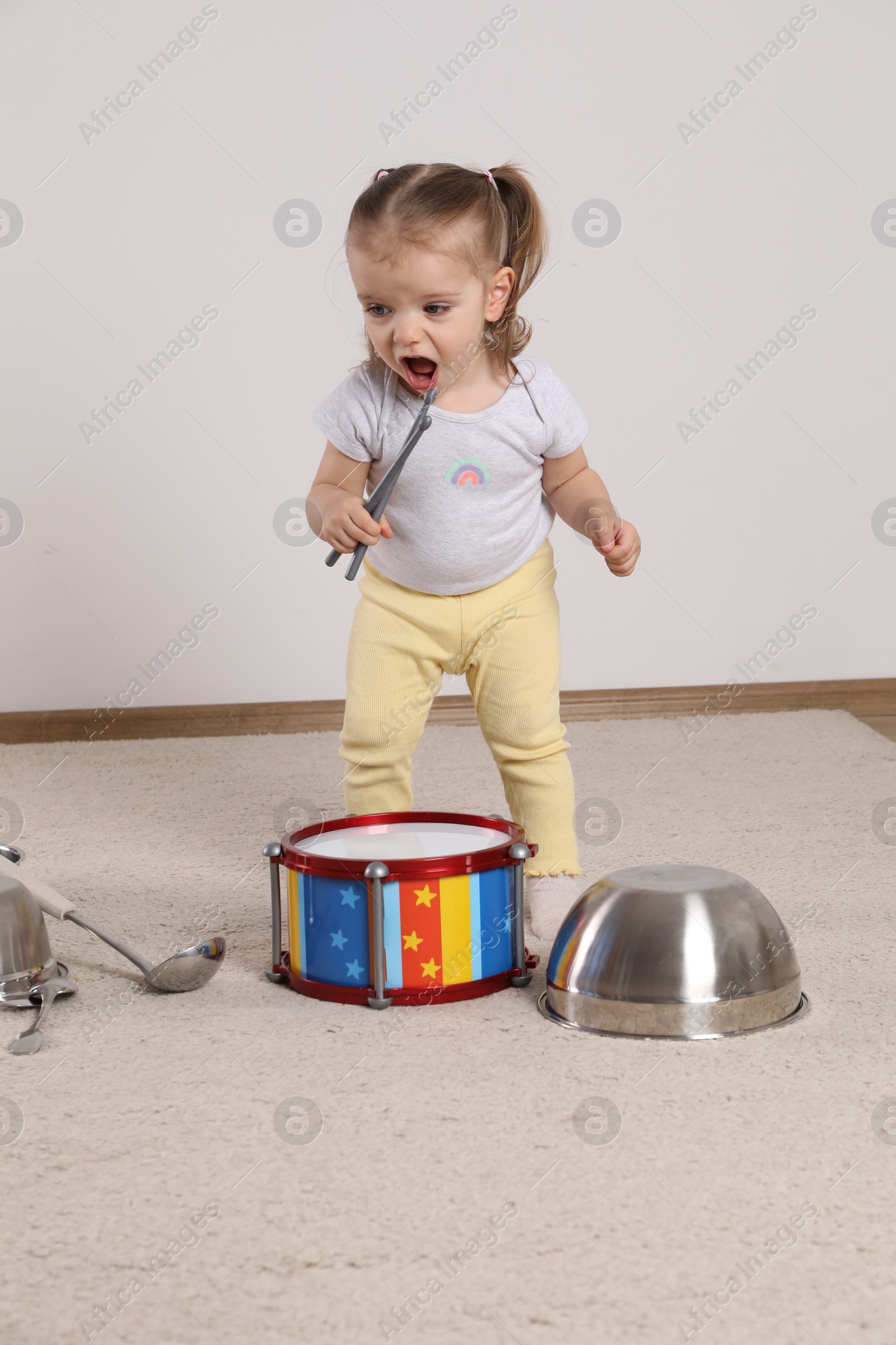 Photo of Cute little girl with cookware and toy drum at home