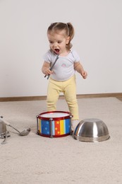 Cute little girl with cookware and toy drum at home