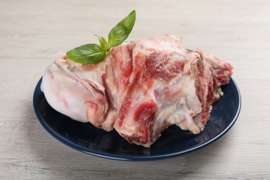 Photo of Plate with raw chopped meaty bones and basil on white wooden table