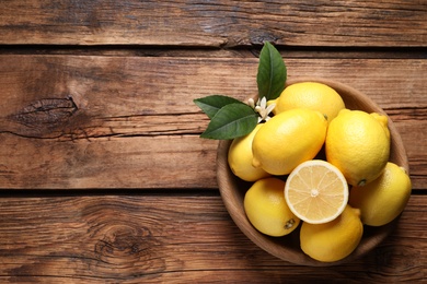 Photo of Many fresh ripe lemons with green leaves and flower on wooden table, top view. Space for text