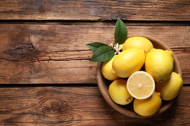 Many fresh ripe lemons with green leaves and flower on wooden table, top view. Space for text