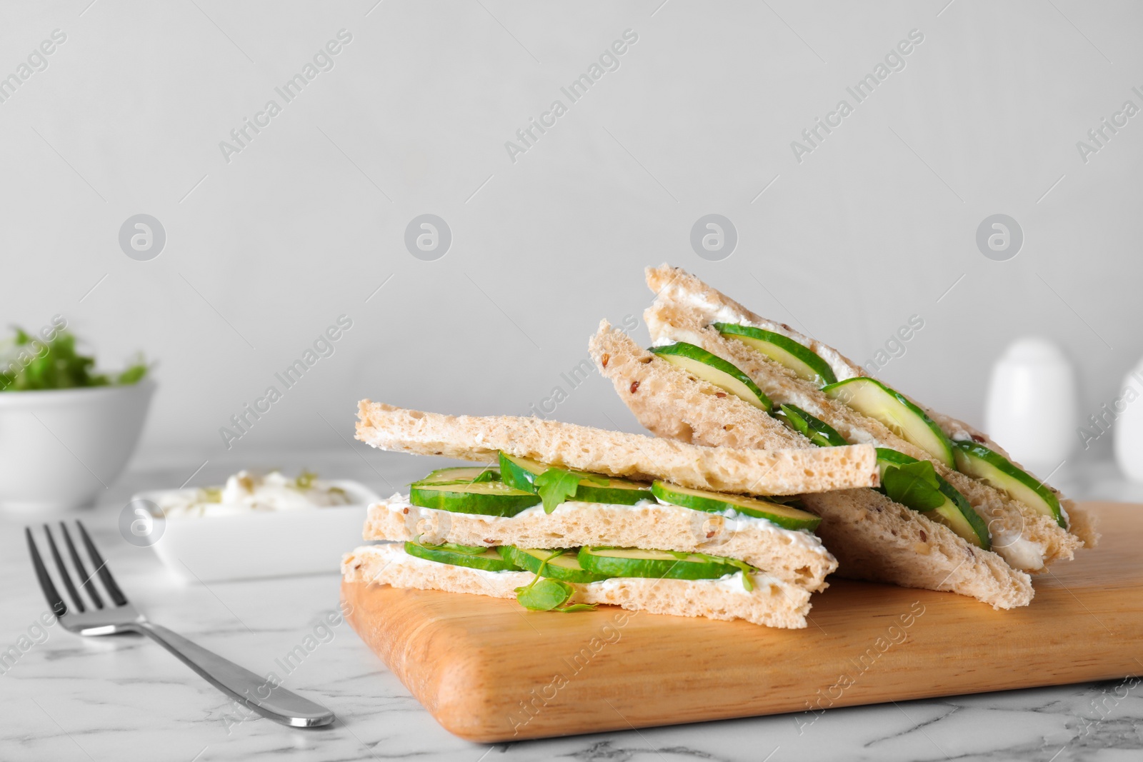 Photo of Wooden board with traditional English cucumber sandwiches on table. Space for text