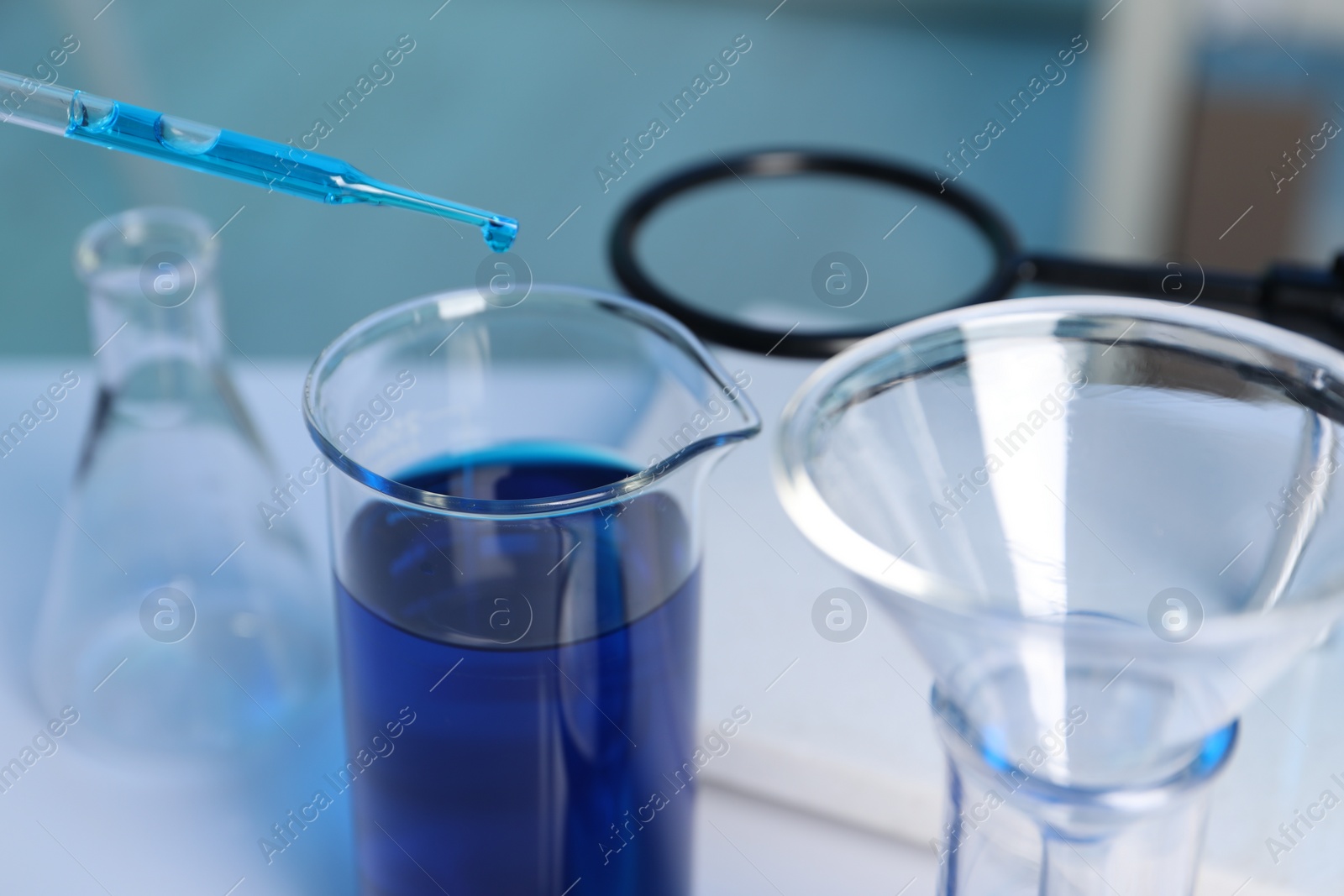 Photo of Laboratory analysis. Dripping blue liquid into beaker on white table, closeup