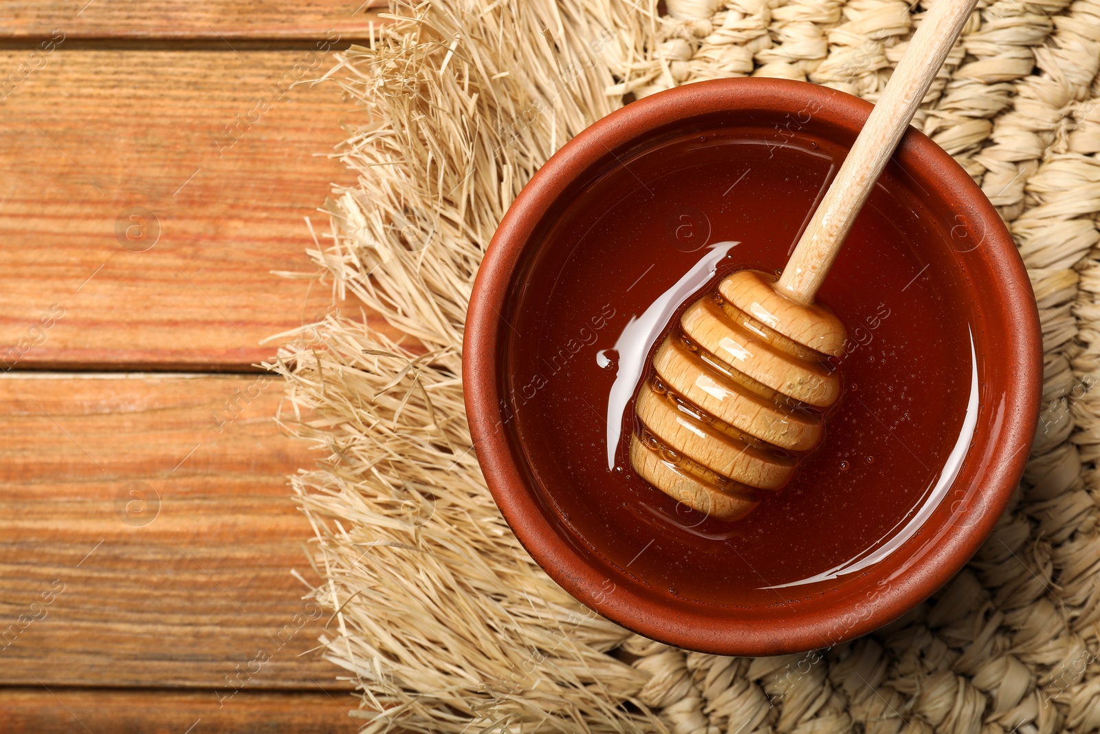 Photo of Dipper with honey in bowl on wooden table, top view. Space for text