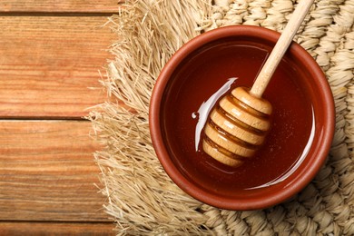 Photo of Dipper with honey in bowl on wooden table, top view. Space for text