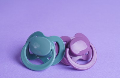 Photo of New baby pacifiers on purple background, closeup