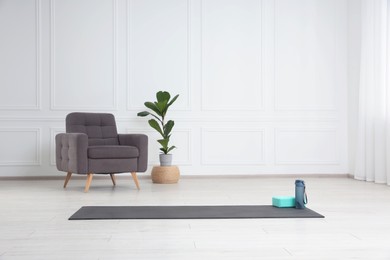 Photo of Exercise mat, yoga block and bottle indoors. Space for text