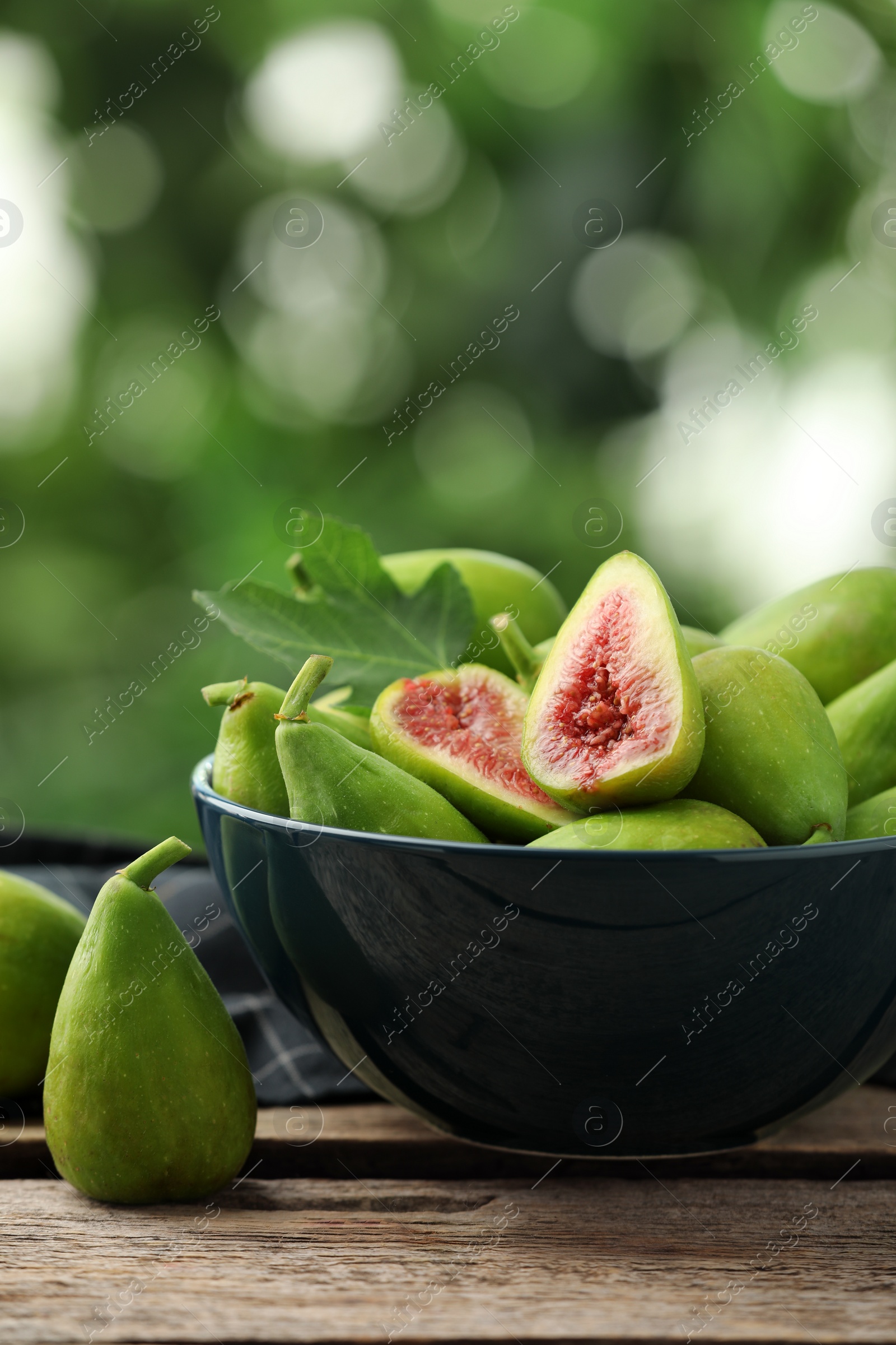 Photo of Cut and whole green figs on wooden table against blurred background, space for text