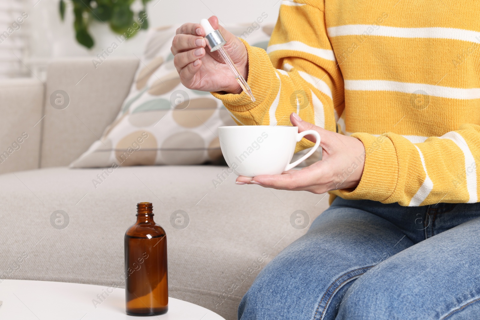 Photo of Woman dripping food supplement into cup at white table indoors, closeup