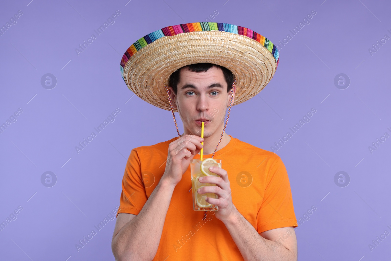 Photo of Young man in Mexican sombrero hat drinking cocktail on violet background