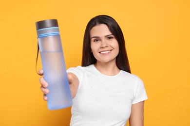 Young woman with bottle of water on orange background